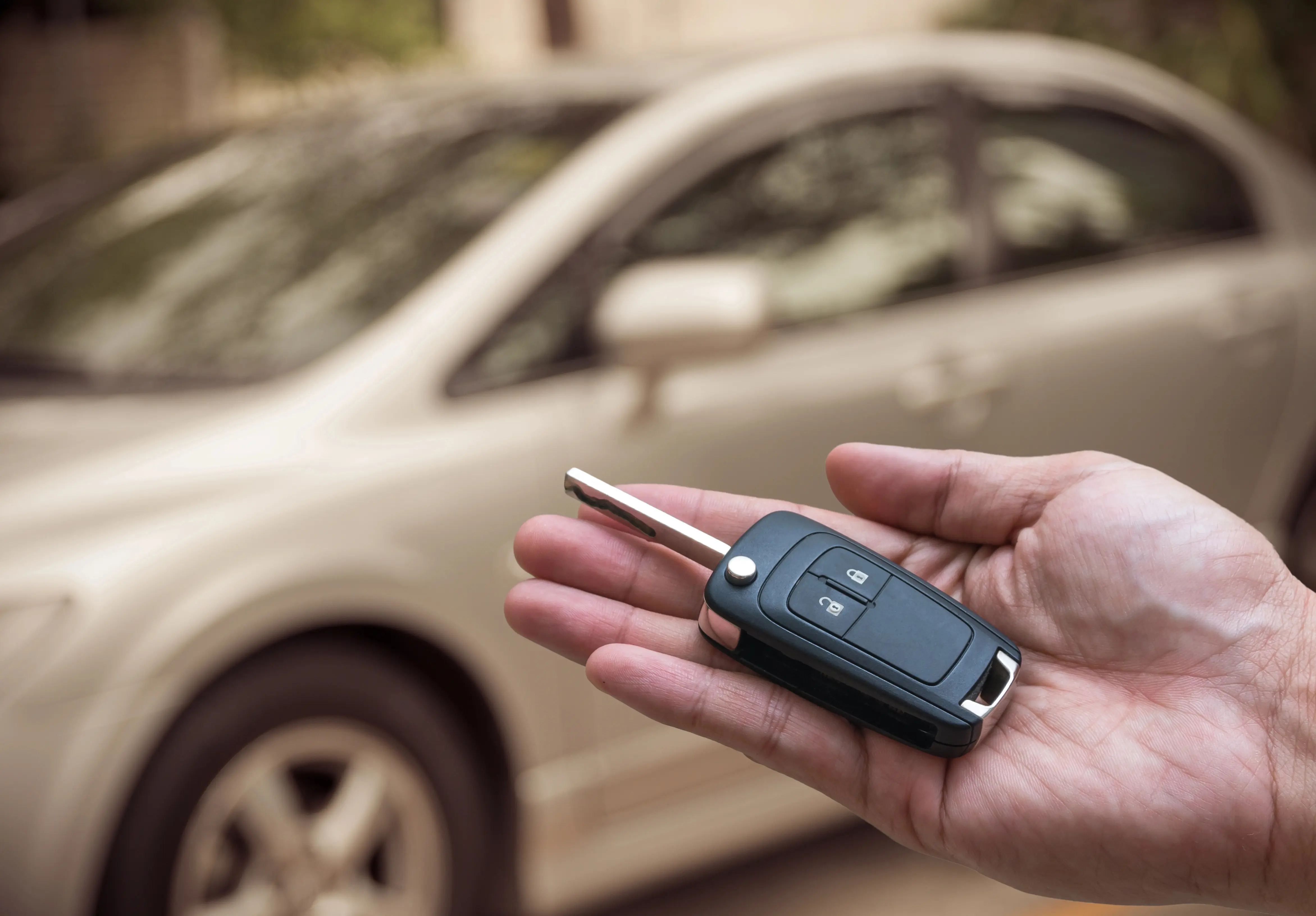 person holding key fob in palm in front of car