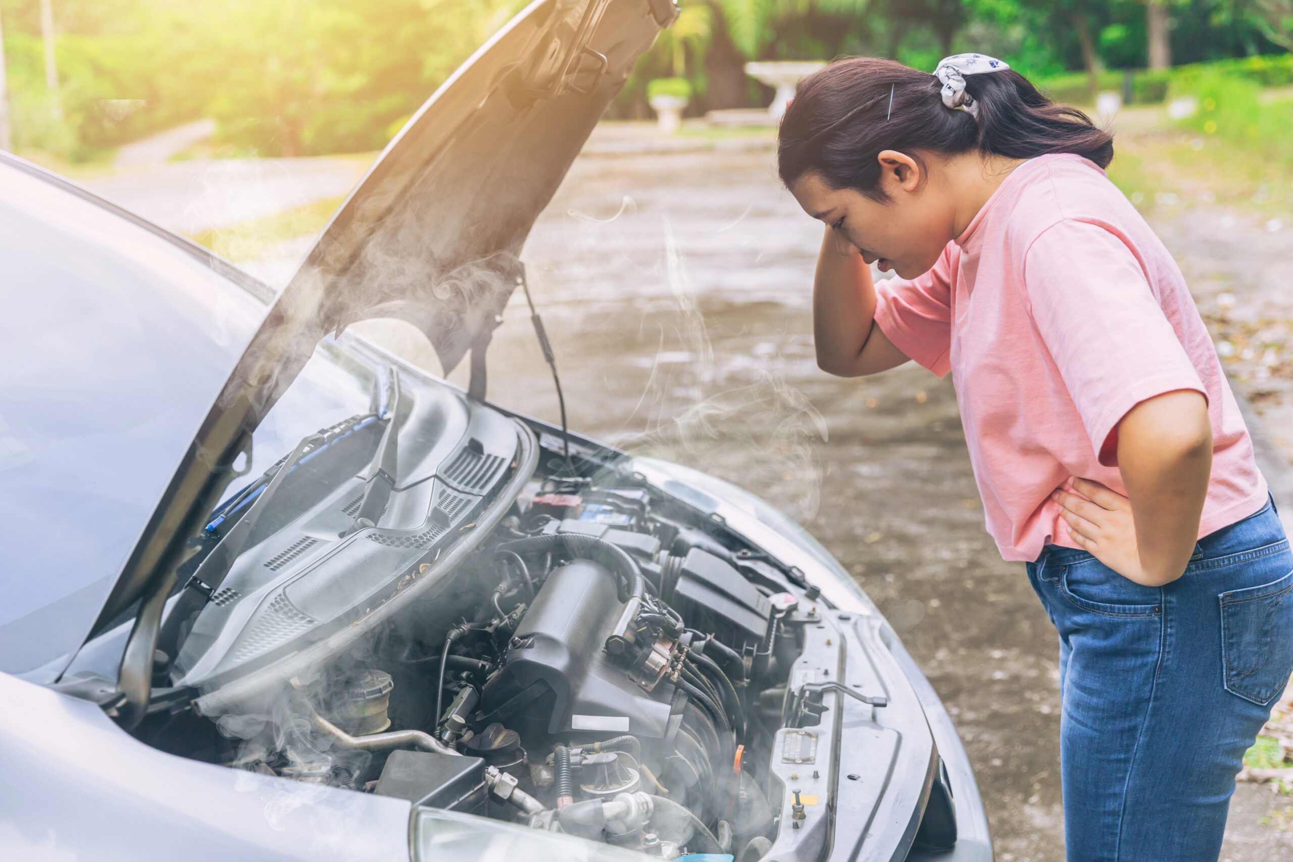 woman looking under hood of car with smoke coming out