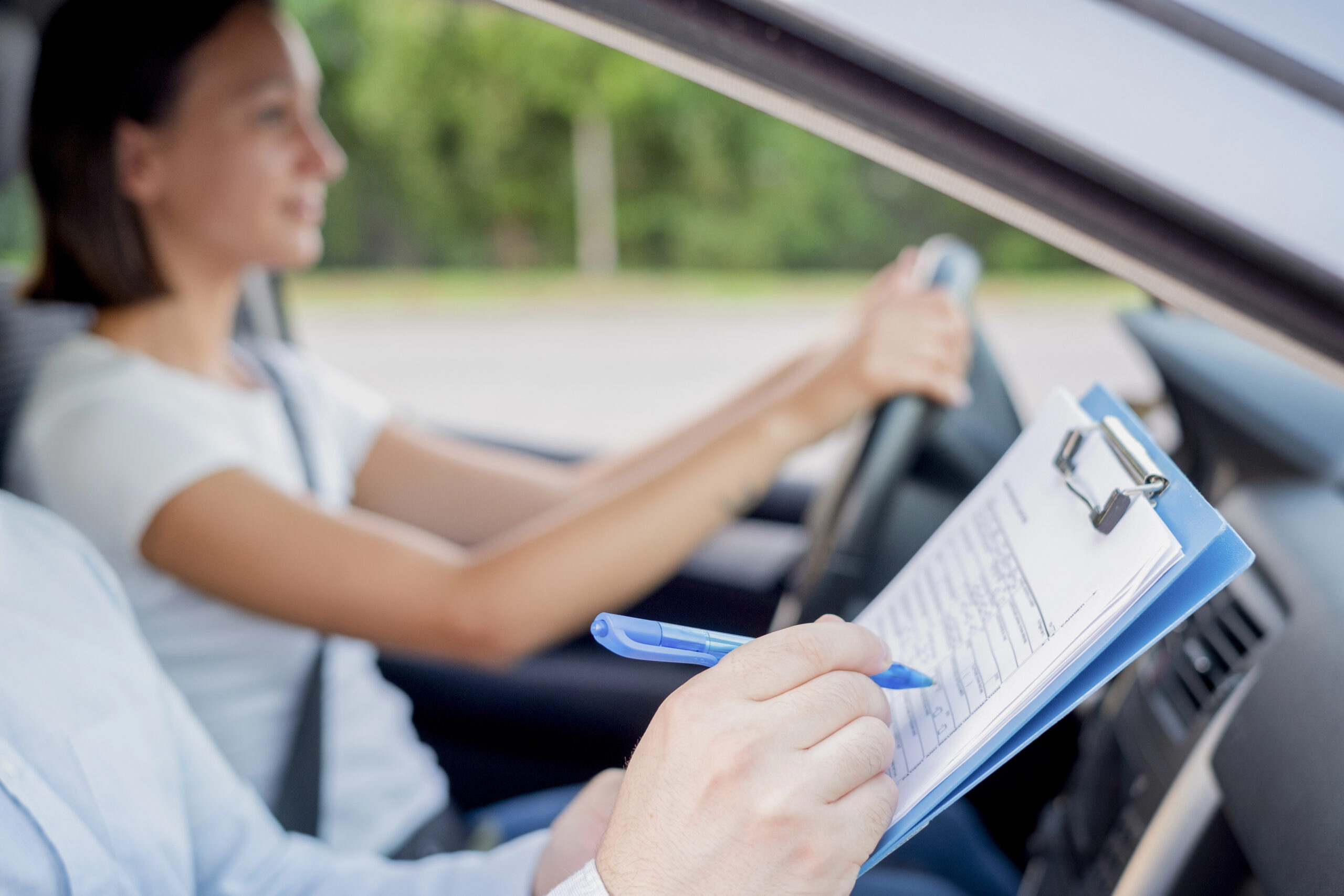 Drive test examiner writing on clipboard while in car with student.