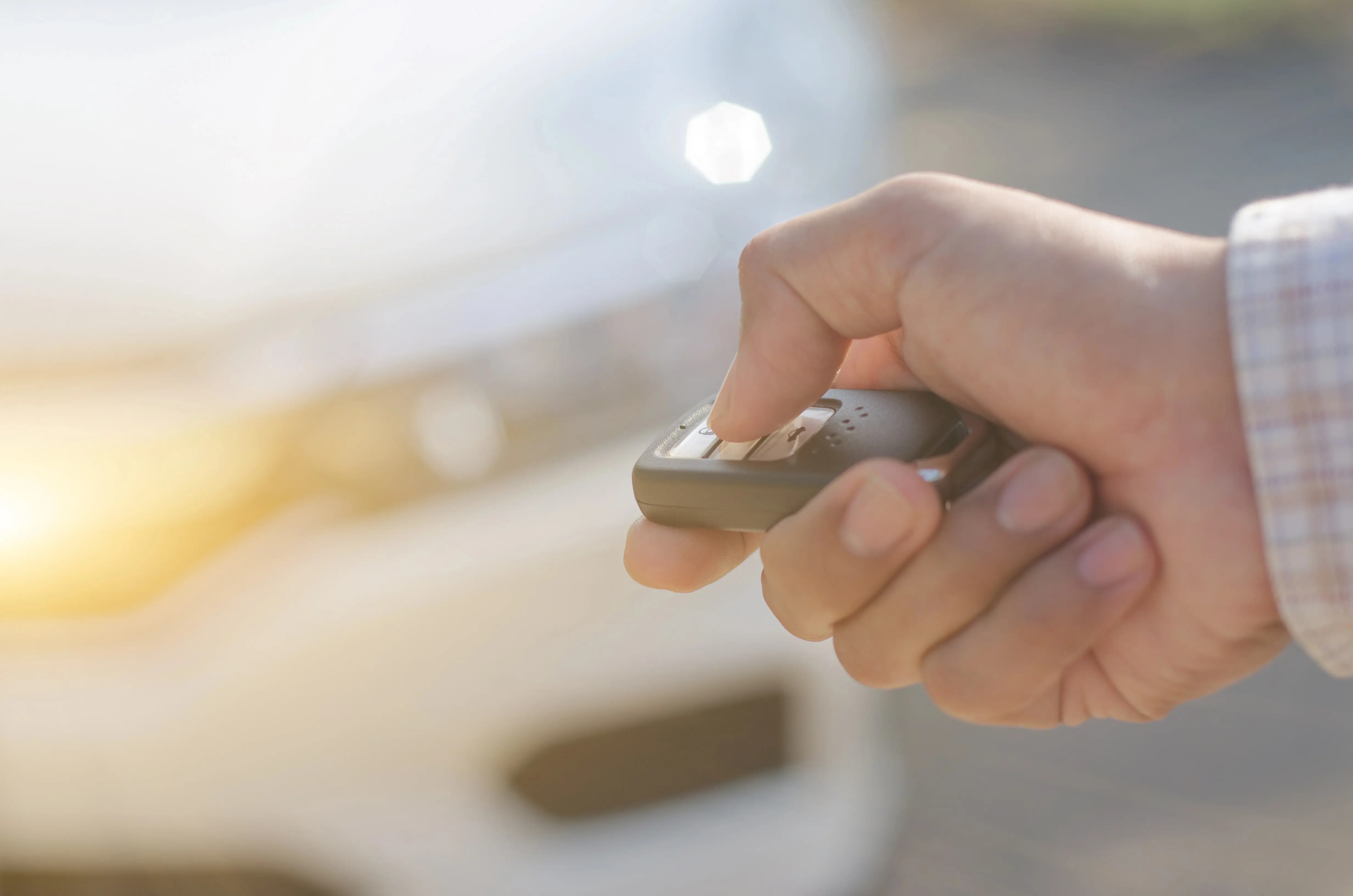 Close-up of hand holding smart key fob in front of car.