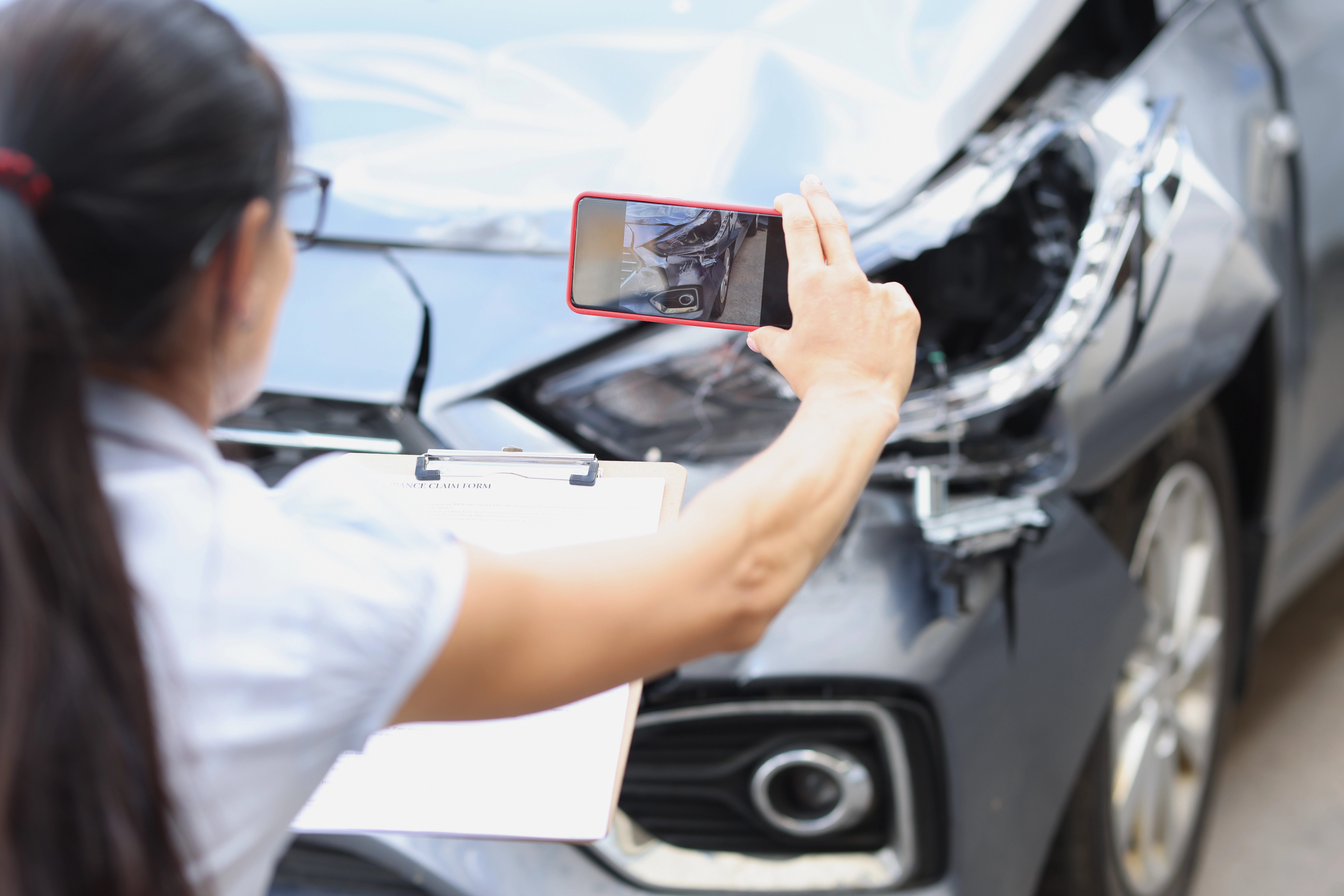 Women taking photo of damaged car on smartphone.