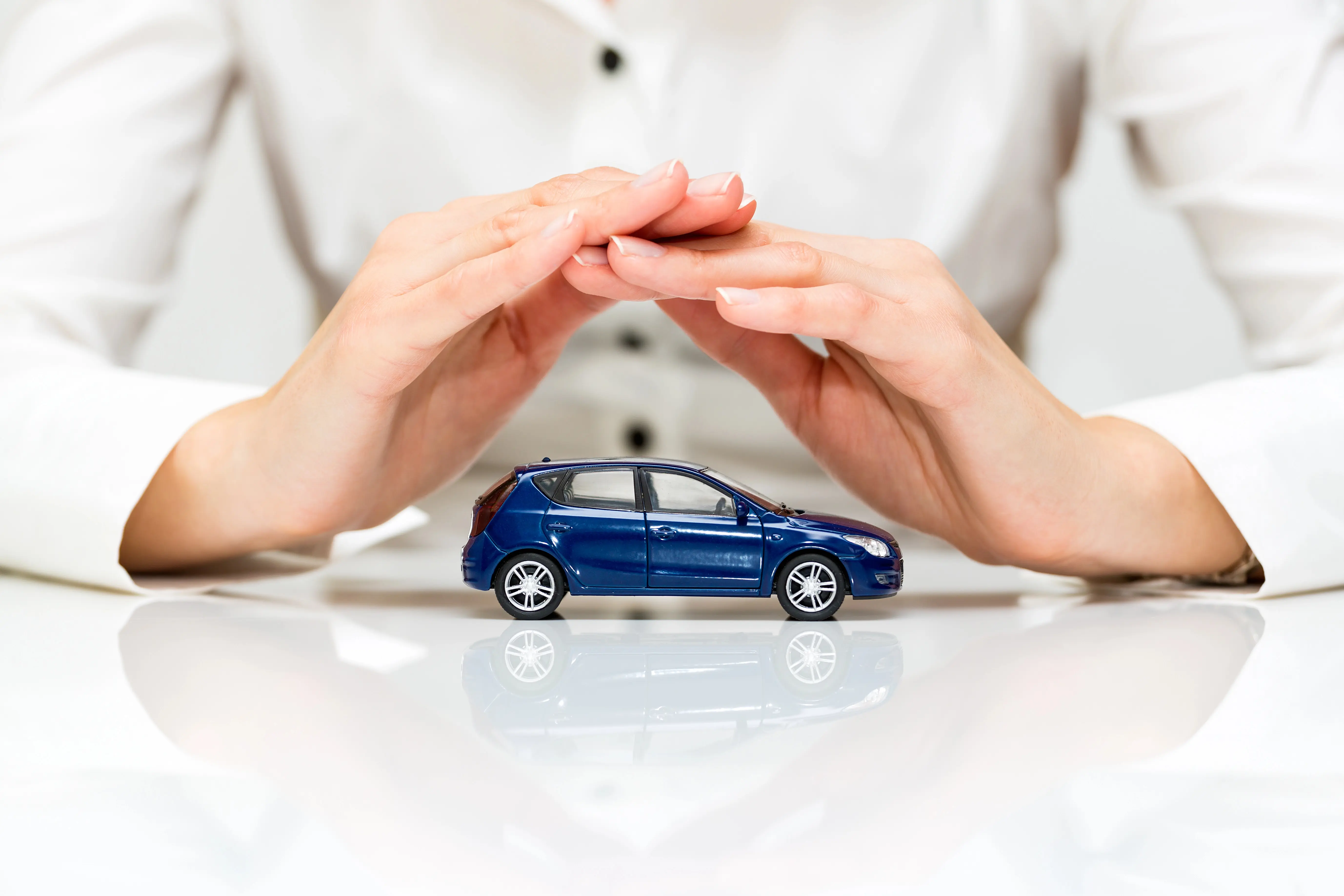 Hands hovering over a small car, symbolizing protection.