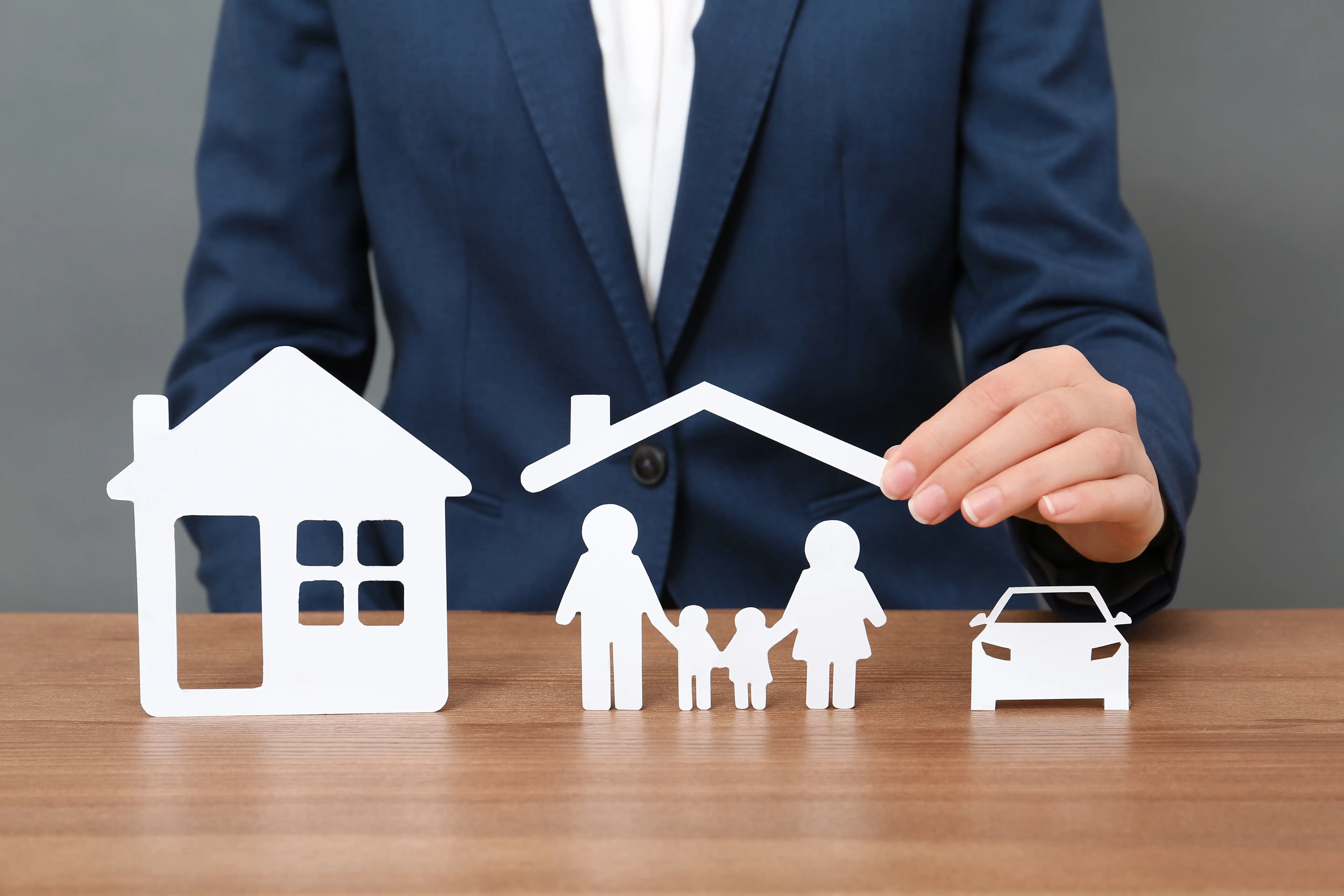 Man in a suit with a cutout house, car, and family holding a protective roof as an umbrella over them